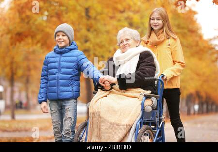 Nette Kinder mit ihrer älteren Großmutter im Rollstuhl im Freien am Herbsttag Stockfoto