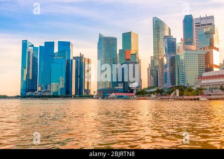 Abend Singapur. Wolkenkratzer am Ufer der Marina Bay. Die Sonne färbte das Wasser golden Stockfoto