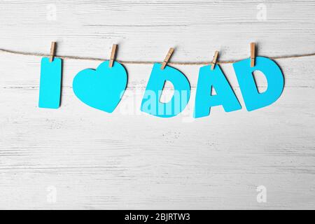 Satz 'I love Dad' aus Papierbuchstaben als Gruß zum Vatertag auf Schnur vor Holzhintergrund Stockfoto
