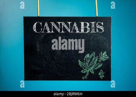 Eine Kreidetafel ist mit den Worten 'Cannabis' und einem Muster von Cannabis auf blauem Hintergrund aufgehängt Stockfoto