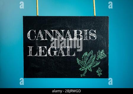 Eine Kreidetafel ist mit den Worten 'Cannabis legal' und einem Muster von Cannabis auf blauem Hintergrund aufgehängt Stockfoto