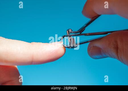 Metall Nagelknipser in der Hand schneiden Sie den Zeigefinger Nagel blauen Hintergrund, Nahaufnahme, Kopierer Raum Stockfoto