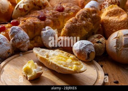 Brot mit geschmolzener Butter und verschiedenen handwerklichen Broten auf einem Holztisch. Stockfoto