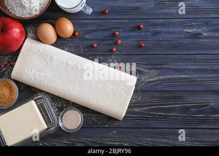 Roher schuppiger Teig und Produkte auf Holzhintergrund Stockfoto