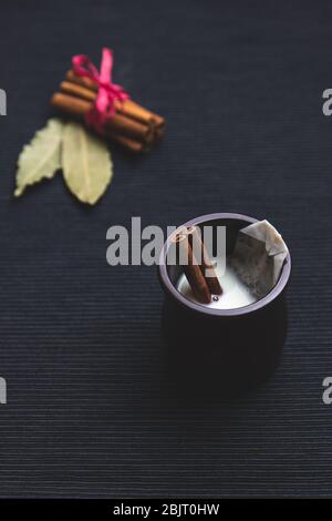 Milchkai-Tee mit Zimt, Teebeutel, schwarzer Tee, in einer braunen Kanne auf schwarzem Hintergrund Stockfoto