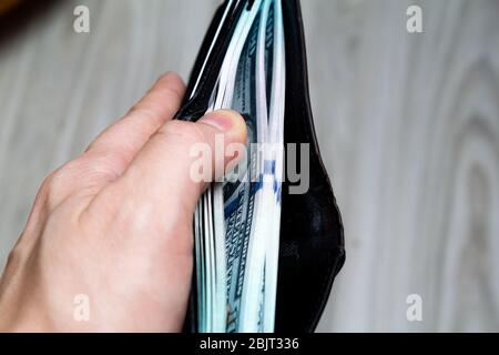 Ein Bündel von hundert Dollar Banknote in einem schwarzen Leder-Geldbörse in der Hand. Blick von der Seite. Nahaufnahme Stockfoto