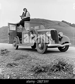 Junge fröhliche Frau sitzt auf dem Dach der Oldtimer auf der Straße Stockfoto