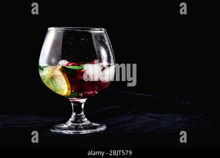 Cocktail mit Eis-Zitronenminze-Erdbeeren in einem Cognac-Glas auf schwarzem Hintergrund Stockfoto