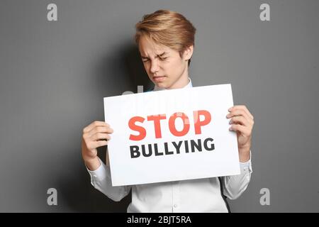 Teenager-Junge mit Schild mit Text 'Stop Mobbing' auf grauem Hintergrund Stockfoto