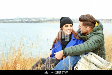 Schönes Paar in warmen Kleidern, das am Flussufer ruht Stockfoto