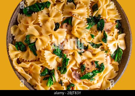 Butterfly Pasta mit gebratenen Pilzen, grüner Spinat in einer Pfanne auf orangefarbenem Hintergrund Stockfoto