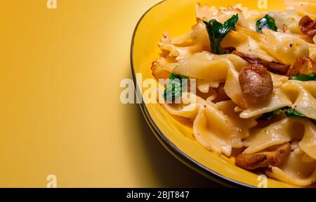 Schmetterling Pasta mit gebratenen Pilzen, grüner Spinat auf einem gelben Teller auf einem orangefarbenen Hintergrund. Copy space Stockfoto