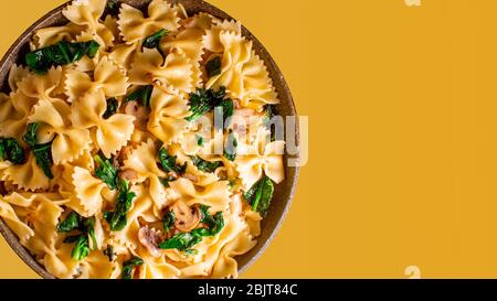 Butterfly Pasta mit gebratenen Pilzen, grüner Spinat in einer Pfanne auf einem orangefarbenen Hintergrund. Copy space Stockfoto