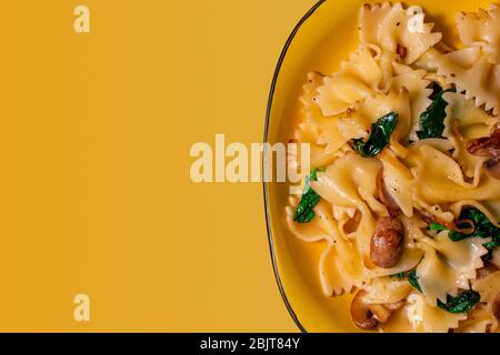 Schmetterling Pasta mit gebratenen Pilzen, grüner Spinat auf einem gelben Teller auf einem orangefarbenen Hintergrund. Copy space Stockfoto