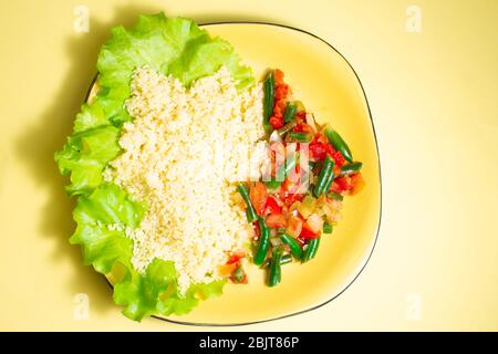 Couscous Brei mit Salat und Gemüse auf einem gelben Teller auf einem gelben Hintergrund gesunde Fitness-Lebensmittel Stockfoto