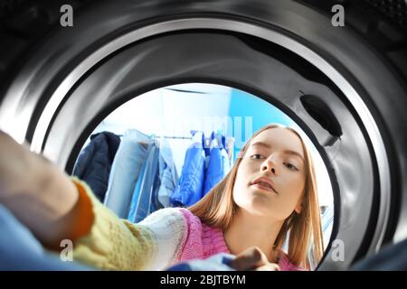 Junge Frau, die Wäsche im Waschsalon macht, Blick von innen von der Waschmaschine Stockfoto