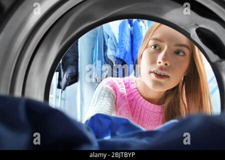 Junge Frau, die Wäsche im Waschsalon macht, Blick von innen von der Waschmaschine Stockfoto