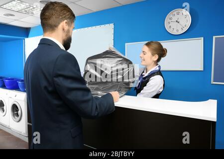 Junger Mann, der seinen sauberen Anzug von einem Wäschereiarbeiter an der Rezeption erhält Stockfoto