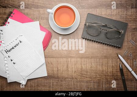 Blatt Papier mit Wort 'Hausaufgaben', Tee und Schreibwaren auf Holzhintergrund, Draufsicht Stockfoto