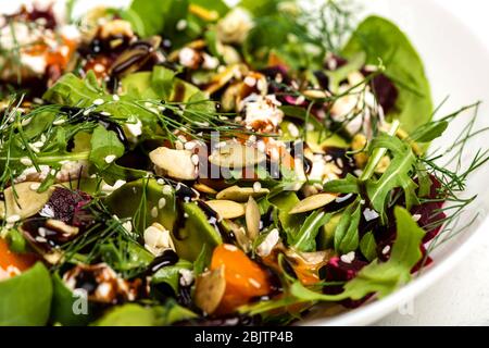 Salat mit Rote Bete, Avocado, Feta, Rucola, Tomaten, verschiedenen Grüns, Kürbiskernen in einer weißen Schüssel. Ernährung gesunde Ernährung zur Gewichtsabnahme. Nahaufnahme. Stockfoto