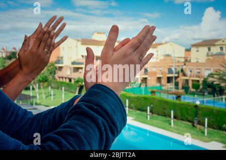 Multirassische Familie applaudiert Gesundheitsmitarbeiter vom Balkon während Coronavirus Confinement. Schwarze und kaukasische Frauen. Stockfoto