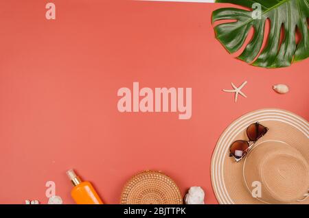 Sommer Strohhut, tropische Monstera Blatt, Sonnenbrille, Muscheln, Sonnencreme, Seesterne auf rotem Hintergrund. Draufsicht, Kopie Raum. Stockfoto