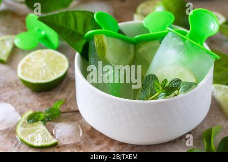 Hausgemachte Eiswürfel aus nächster Nähe mit Limettensaft und Minze, Mojito-Fruchteis auf einem hellen Stein- oder Schieferhintergrund. Stockfoto