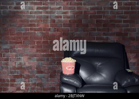 Kino Sessel mit Popcorn und Fernbedienung für Home Entertainment auf Backstein Wand Hintergrund. Filme ansehen Stockfoto