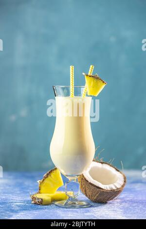 Ein Glas leckerer gefrorener Pina Colada traditioneller karibischer Cocktail mit Ananasscheibe, serviert auf blauem Betongrund. Stockfoto