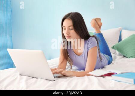 Nettes Teenager-Mädchen mit Laptop während Hausaufgaben im Schlafzimmer Stockfoto