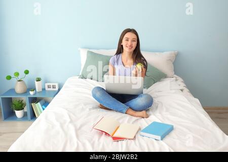 Nettes Teenager-Mädchen mit Laptop während Hausaufgaben im Schlafzimmer Stockfoto