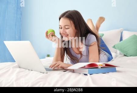Nettes Teenager-Mädchen mit Laptop während Hausaufgaben im Schlafzimmer Stockfoto
