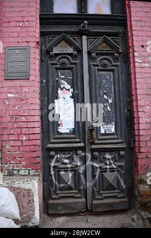 Eingang zu verlassenen historischen Gebäude mit alten Holztür mit verzierten schwarzen Paneelen an roten Ziegelwand. Architektonische Details eines baufälligen Gebäudes Stockfoto