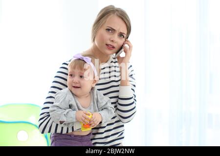 Junge Kindermädchen hält Mädchen beim Sprechen auf Handy, drinnen Stockfoto