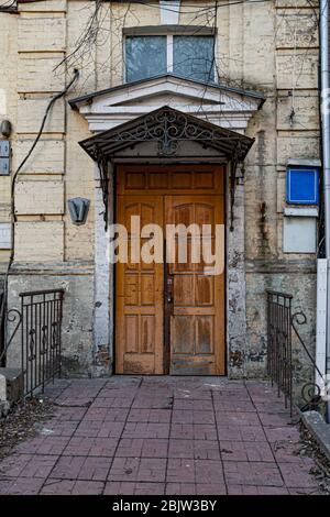 Antike verzierte Metallveranda und alte Holztür in Ziegelwand. Architektonische Details des gelben Steingebäudes. Stockfoto