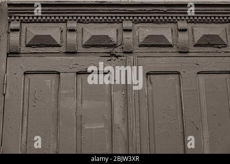 Sepia getöntes Foto von verzierten Laubsägemuster der alten Holztür mit abblätternder Farbe. Rahmen und Schnitzelemente der Türverkleidungen des klassischen Gebäudes in Stockfoto