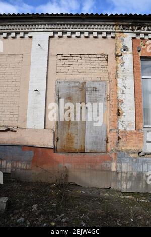 Die Mauer aus gemauerten Ziegelsteinen des verlassenen Gebäudes mit weißen falschen Säulen und einer verschlossenen Tür aus rostetem Metall. Die Fassade des Hauses musste renoviert werden Stockfoto