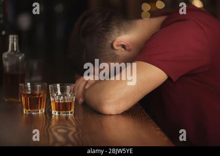 Bewusstloser betrunkener Mann mit Gläsern Getränk in der Bar. Alkoholismus Problem Stockfoto