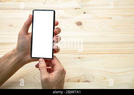 Mockup für den Bildschirm des Mobiltelefons. Mann mit einem Smartphone mit leerem weißen Bildschirm, Holzhintergrund, Kopierraum Stockfoto