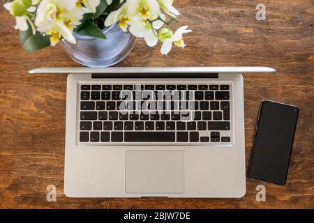 Arbeitsplatz. Computer-Laptop und Mobiltelefon auf einem Schreibtisch aus Holz, Work-from-Home-Konzept, Draufsicht Stockfoto