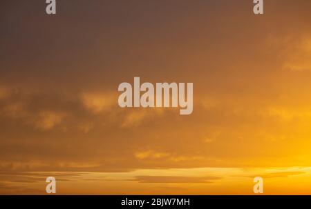 Himmel bei Sonnenuntergang. Sonnenaufgang malt mit orangefarbenen Schattierungen den wolkigen Himmelshintergrund. Stockfoto