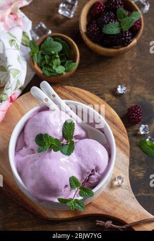 Hausgemachte Bio-Eiscreme mit Minze. BlackBerry Eis in weißer Schüssel auf einem rustikalen Tisch. Stockfoto
