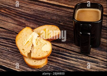 Frischer Weizentoast mit Butter und einem Keramikbecher mit Kaffee mit Milch auf Holzgrund. Nahaufnahme Stockfoto