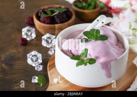 Hausgemachte Bio-Eiscreme mit Minze. BlackBerry Eis in weißer Schüssel auf einem rustikalen Tisch. Stockfoto