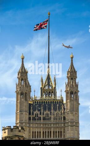 LONDON, ENGLAND - JUNI 2018: Der Victoria Tower im Palace of Westminster mit der Union Jack Flagge und einem vorbeifliegenden Jet