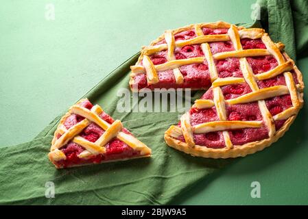 Leckere Himbeerkuchen mit Gitterkruste und einer Scheibe auf einer grünen Serviette. Klassisches Dessert. Sommerkuchen. Einfachste Torte. Himbeerkuchen mit einer Teigkruste Stockfoto