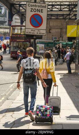 LONDON, ENGLAND - JULI 2018: Junge Touristen, die eine Straße im Zentrum Londons entlang gehen, ziehen Koffer Stockfoto