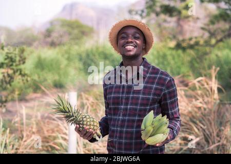 Afrikanischer Bauer Mann hält Ananas und Banane auf Bio-Farm mit Lächeln und glücklich.Landwirtschaft oder Anbaukonzept Stockfoto