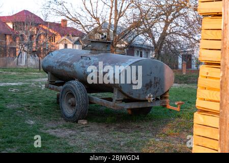 Rostiger alter großer Lauf auf Rädern. Zerbrochener Behälter für Flüssigkeiten, der auf dem Hinterhof im Dorf steht. Stockfoto