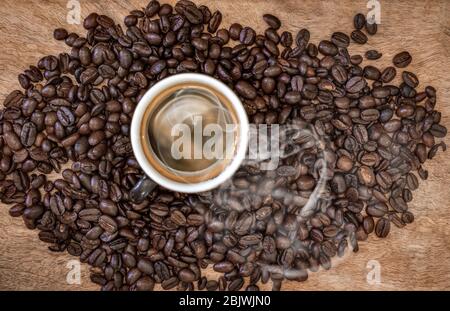 Eine Gruppe gerösteter Kaffeebohnen mit einer Tasse Kaffee in der Mitte, aus der Rauch aussengt Stockfoto